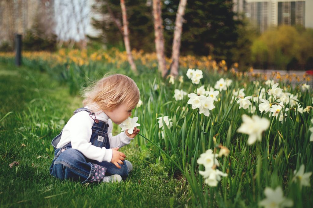 girl sitting on grass smelling white petaled flower